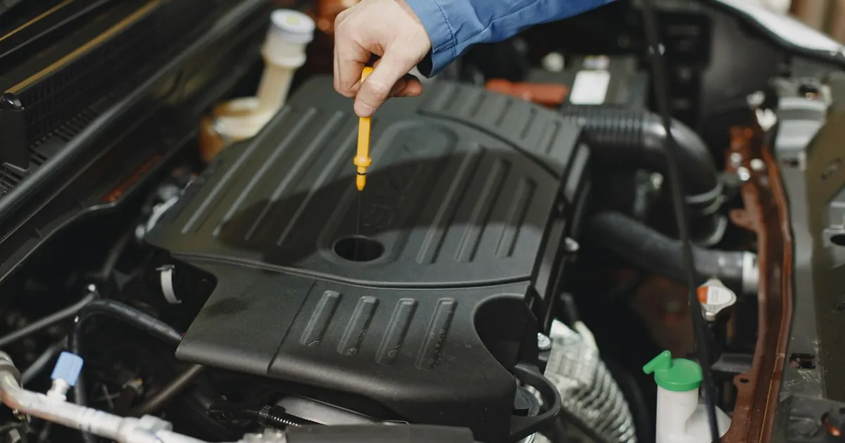 Close-up of a person checking engine oil using a dipstick in a car's engine bay.