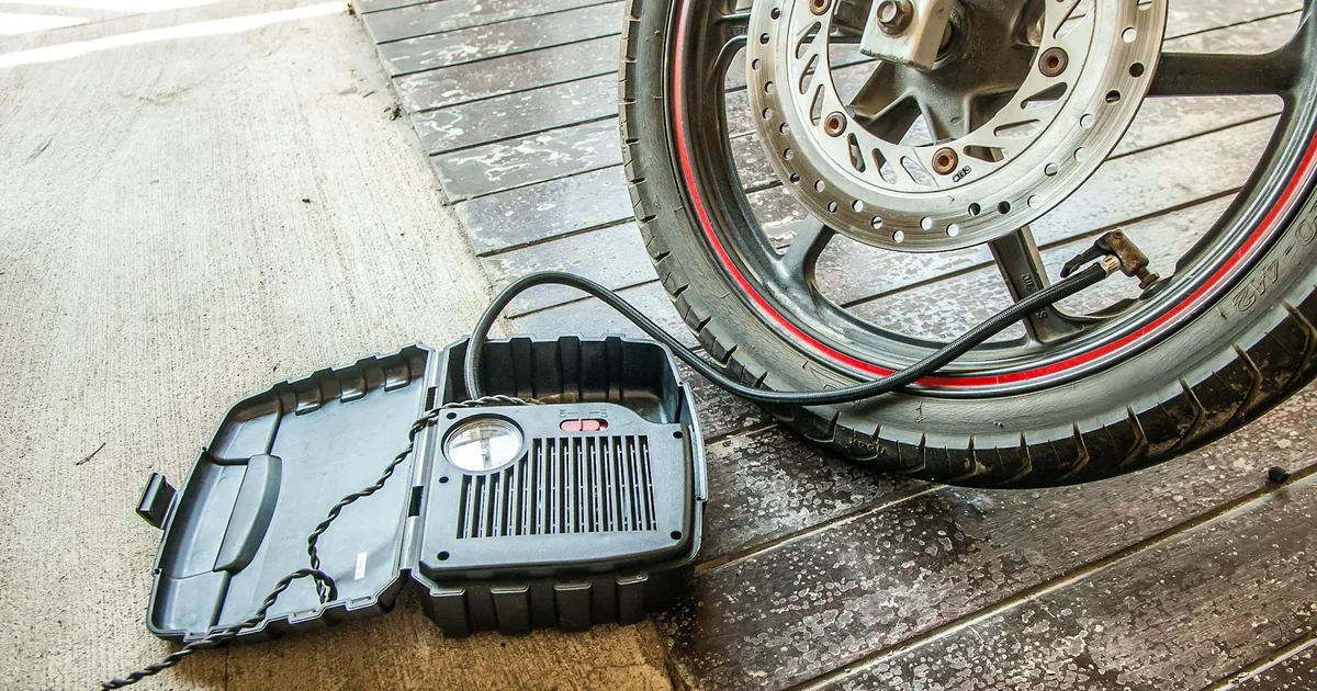 Close-up of a motorcycle tire being inflated using a portable air pump.