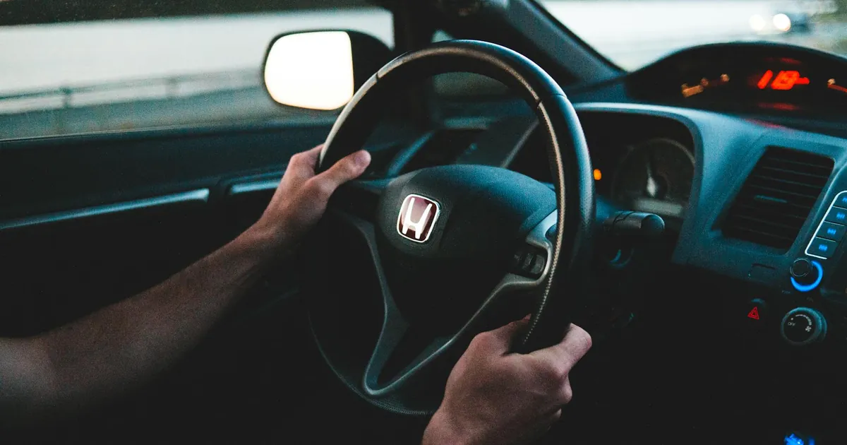 Crop unrecognizable man driving contemporary auto near lake under white sky in evening