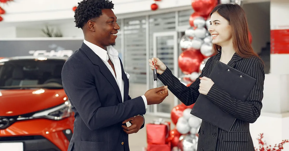 A car dealer handing over keys to a satisfied customer at a decorated dealership.