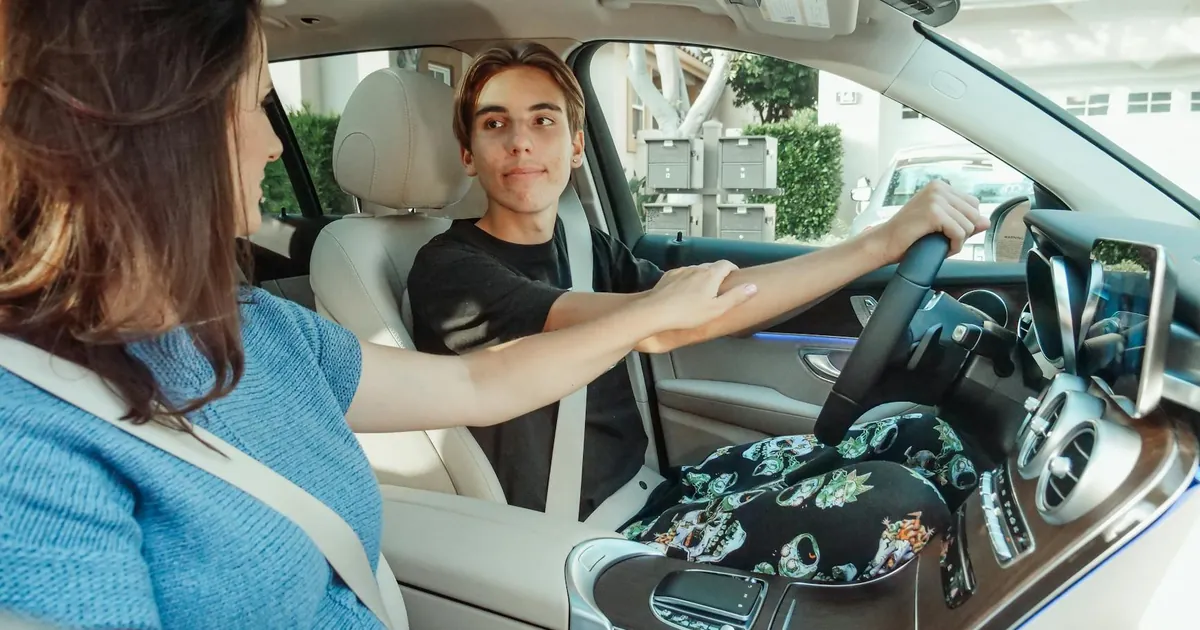 A mother supports her teenage son as he learns to drive in a car