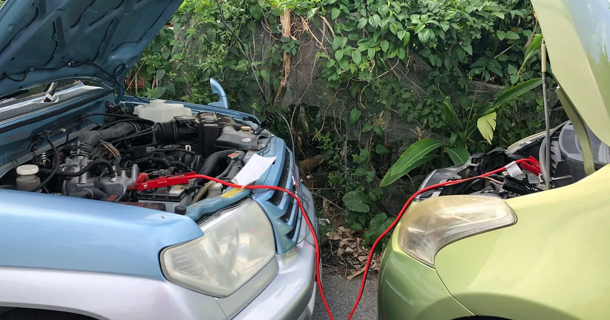 Two cars connected by jumper cables in a parking lot for a battery charge.