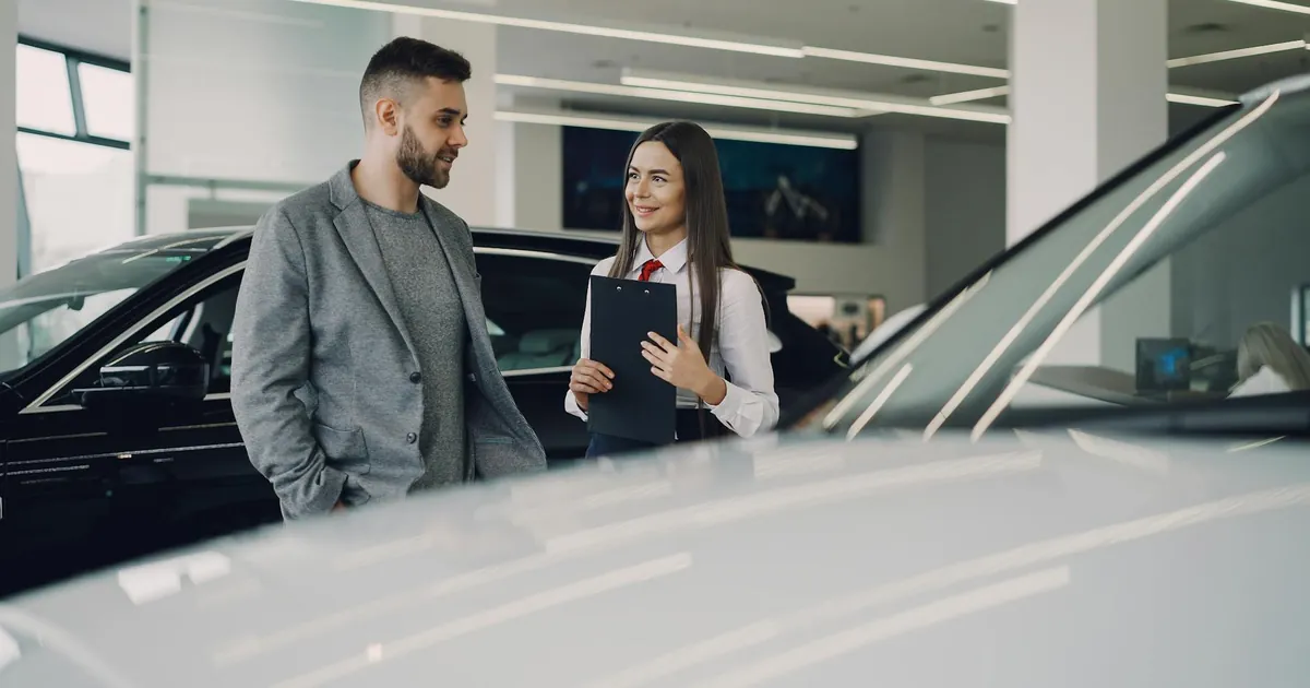Man consults with salesperson in modern car dealership showroom.