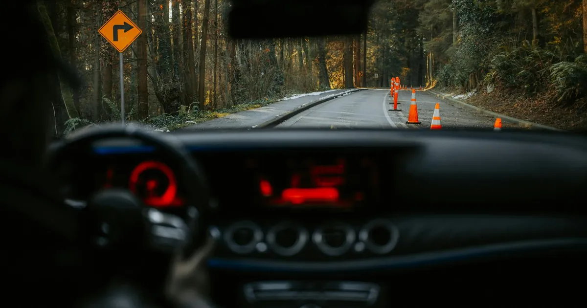View from car dashboard of rural road with traffic cones and turn sign. Scenic forest driving experience.