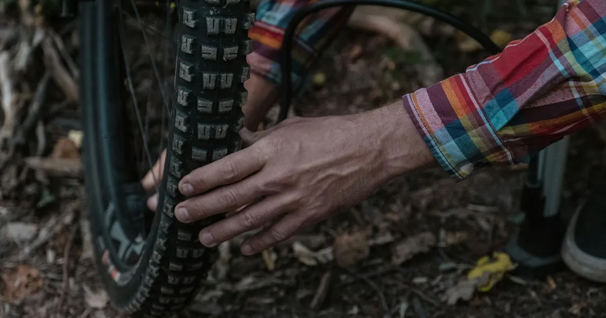 Person in plaid shirt inflating a mountain bike tire in a natural setting, highlighting maintenance and adventure.