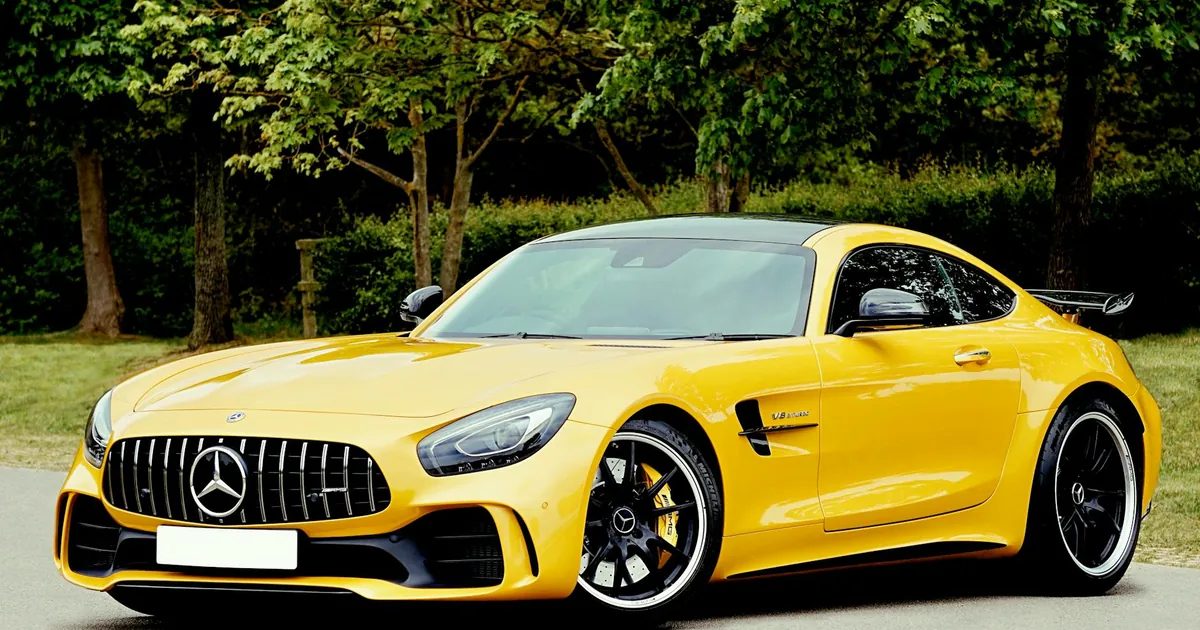 An elegant yellow sports car parked outdoors in a park setting, surrounded by lush greenery.