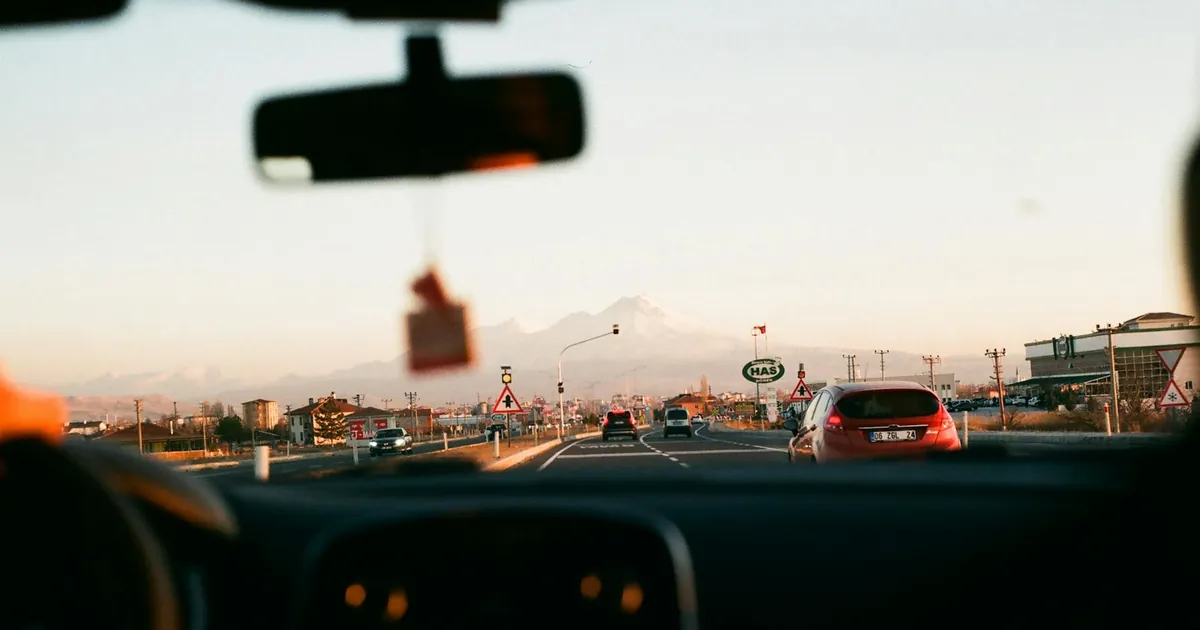 View from inside a car driving towards a mountainous landscape during sunset with beautiful sky.