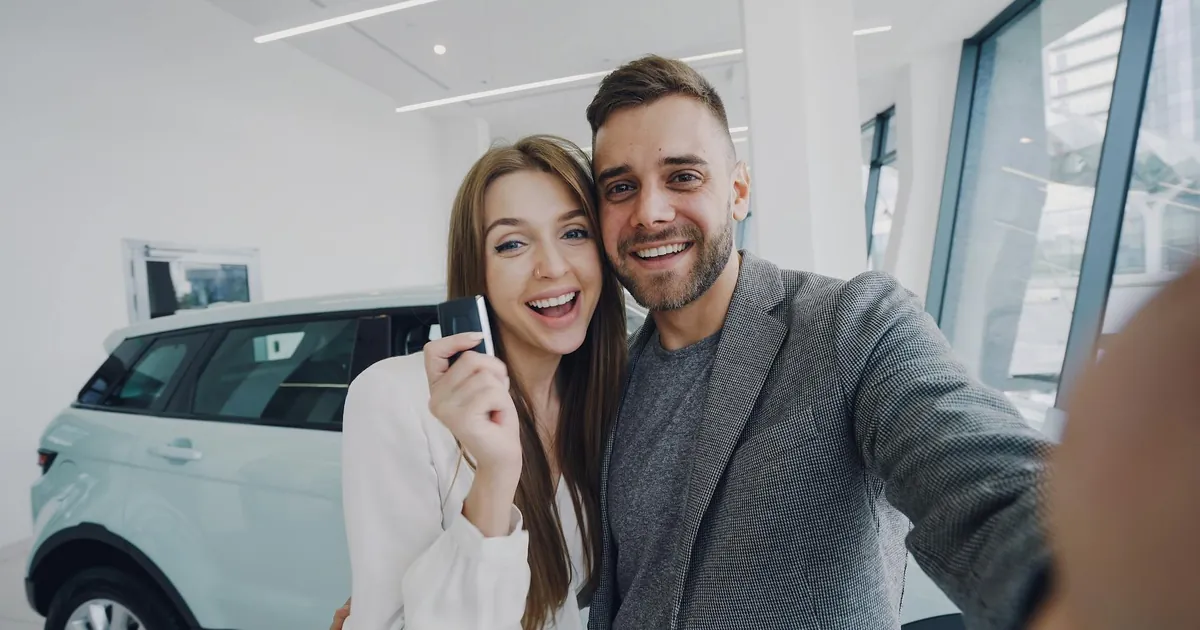 A joyful couple taking a selfie after purchasing a new car, indoors.