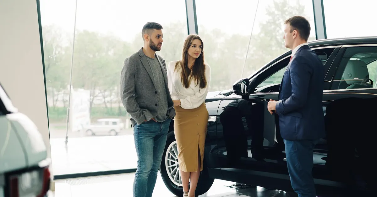 A couple converses with a salesperson about buying a car inside a dealership.