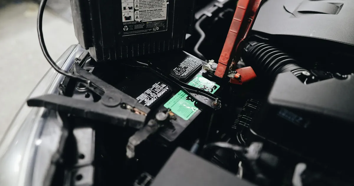 Detailed view of a car battery being jump-started with cables in an engine bay.