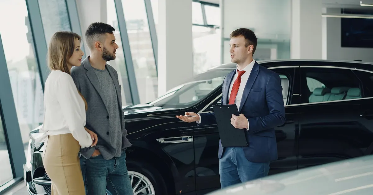 A couple talks with a salesman in a modern car showroom, considering a vehicle purchase.