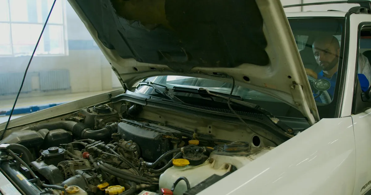 Mechanic checking car engine under open hood in a garage setting.