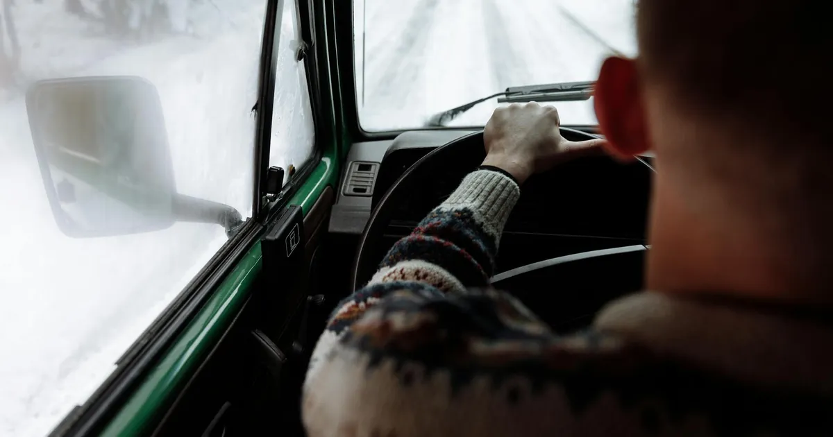 Experience driving on a snowy road with a person in a cozy sweater enjoying the winter view.