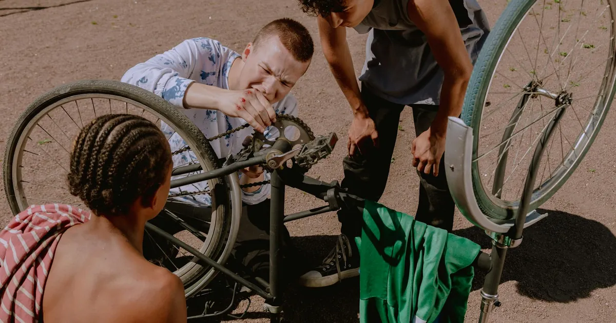 Three young men fixing a bike outdoors on a sunny day, teamwork and repair concept.