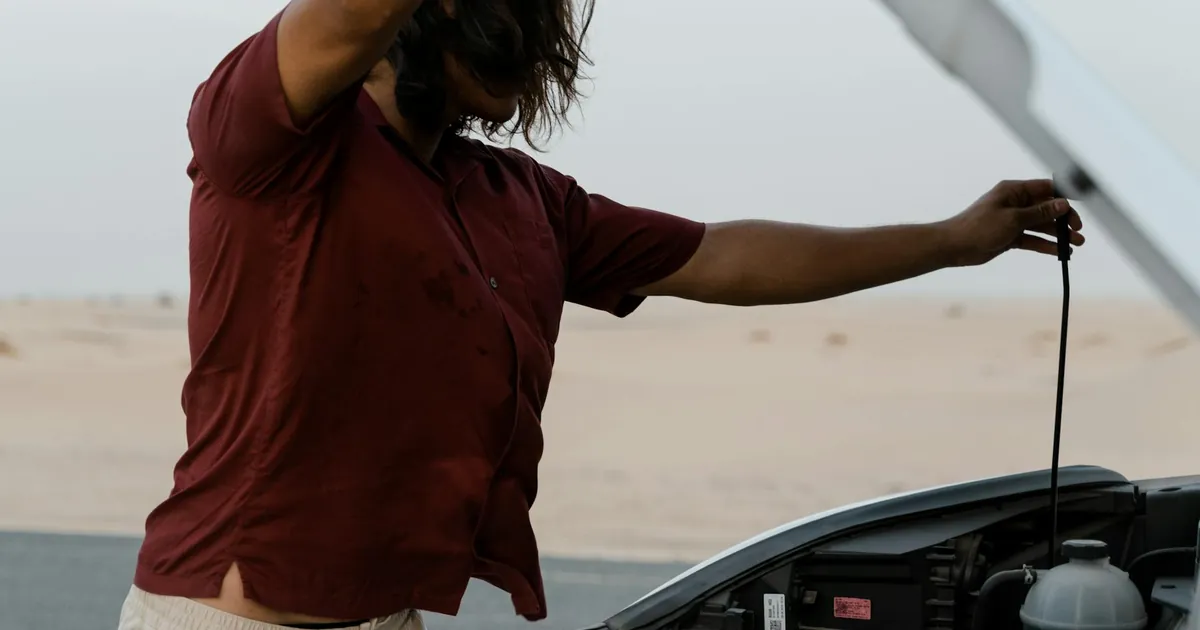 A man examines the engine of a car on a deserted road, highlighting automotive maintenance.