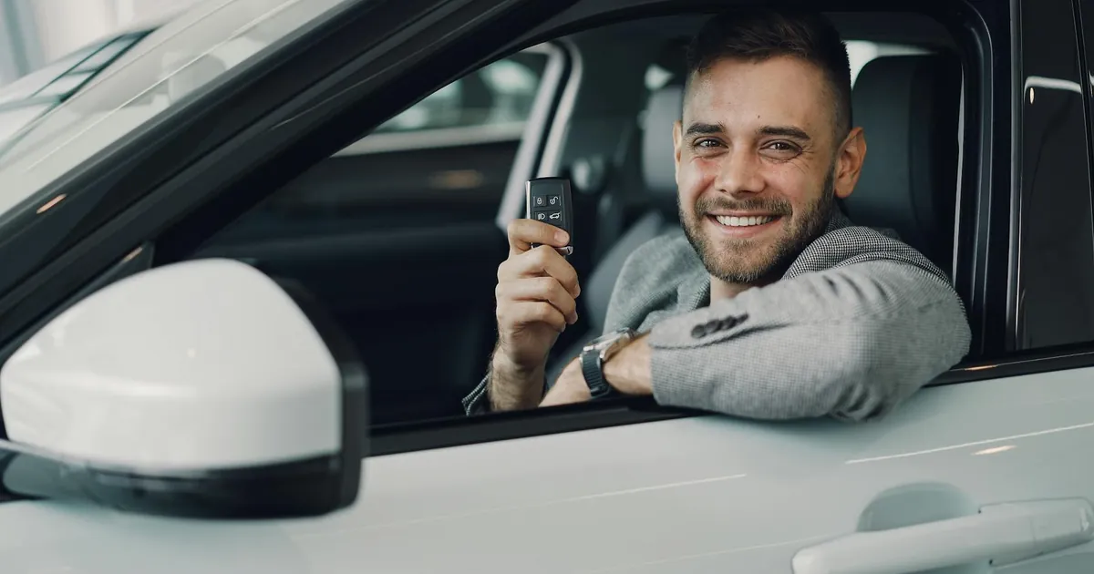 Happy young man holding car keys inside a vehicle. Perfect image for car rental or sales.