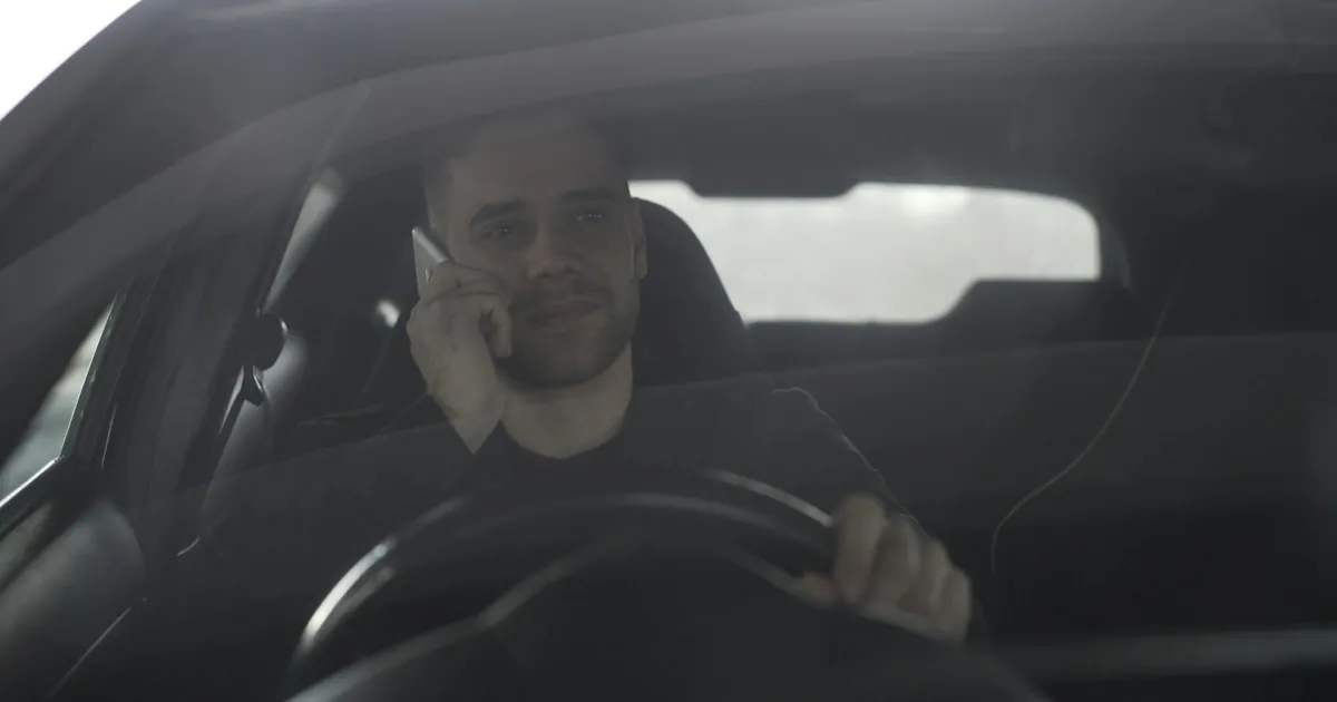 Man talking on mobile phone while driving, seen through car windshield.