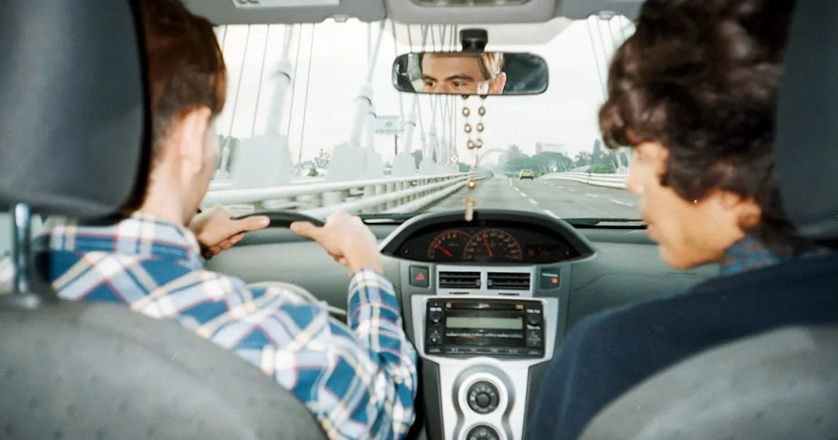 A man driving a car with another man in the back seat