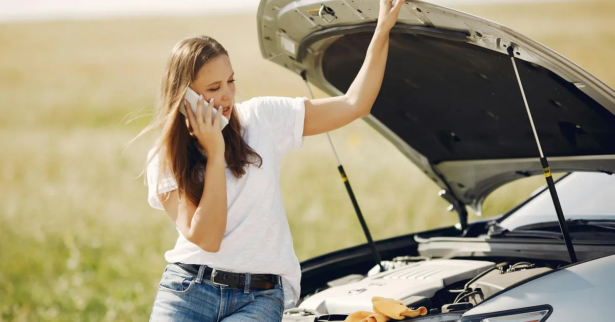 Young woman on phone seeking help for car breakdown on a sunny day.
