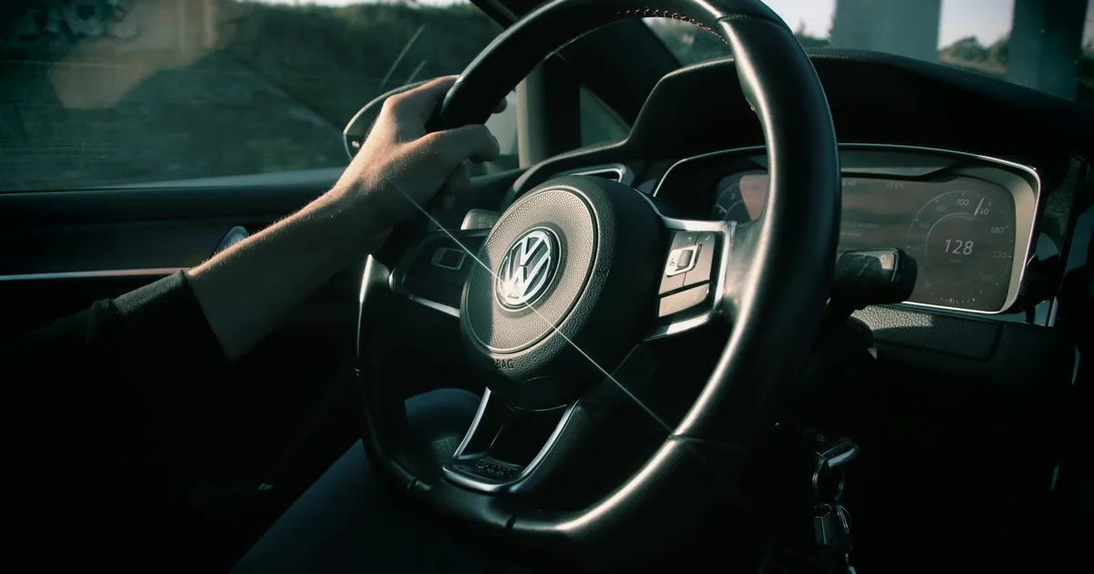 Close-up view of a driver's hands on a Volkswagen steering wheel in a moving car.