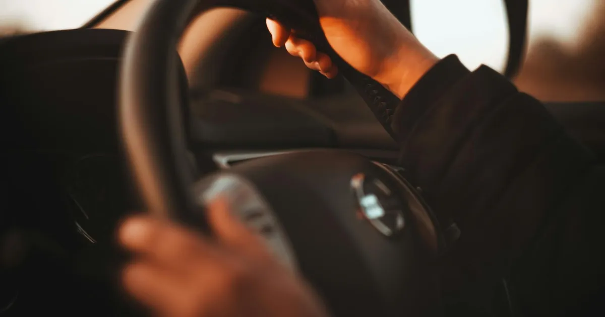 Close-up of a person's hands gripping a steering wheel in warm sunset light. Interior car focus.