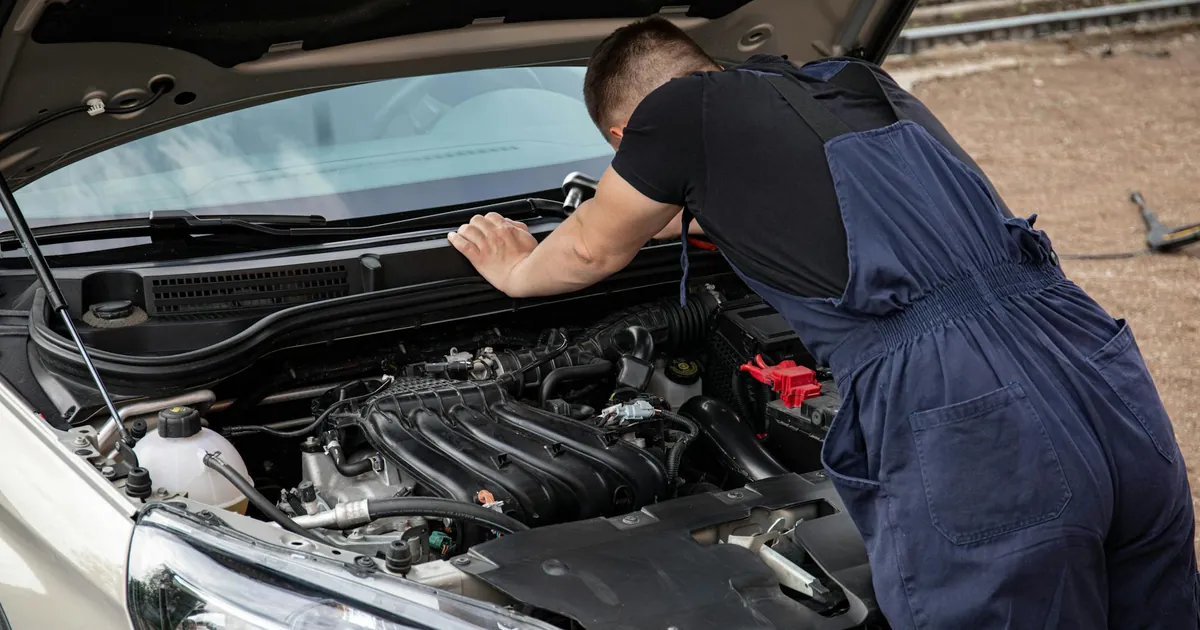 Mechanic checking car engine outdoors, focusing on vehicle maintenance and repair.