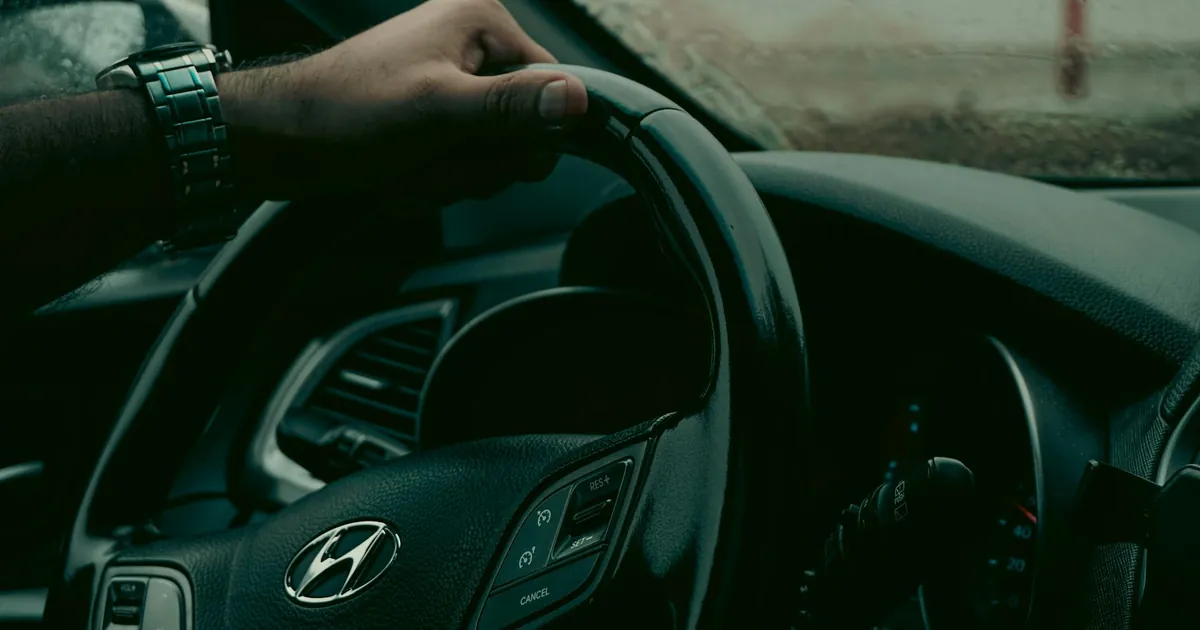 A person drives a car focusing on the steering wheel and dashboard in view.