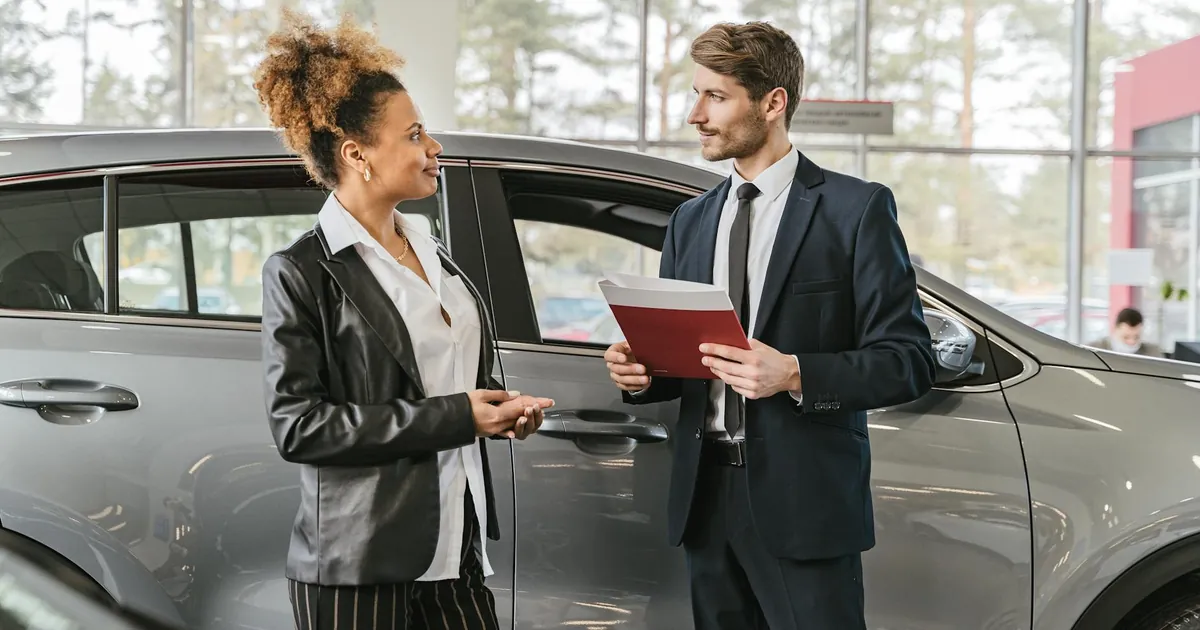 A woman discussing car purchase with a dealer inside a car dealership showroom.