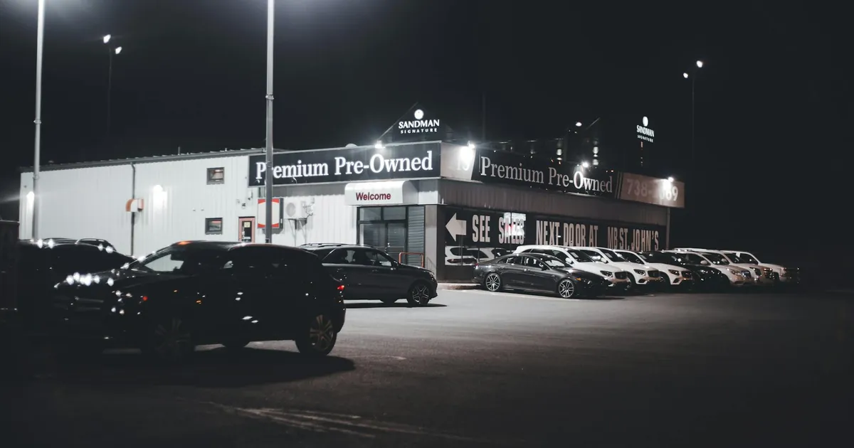 Illuminated car dealership lot showcasing premium pre-owned vehicles at night.