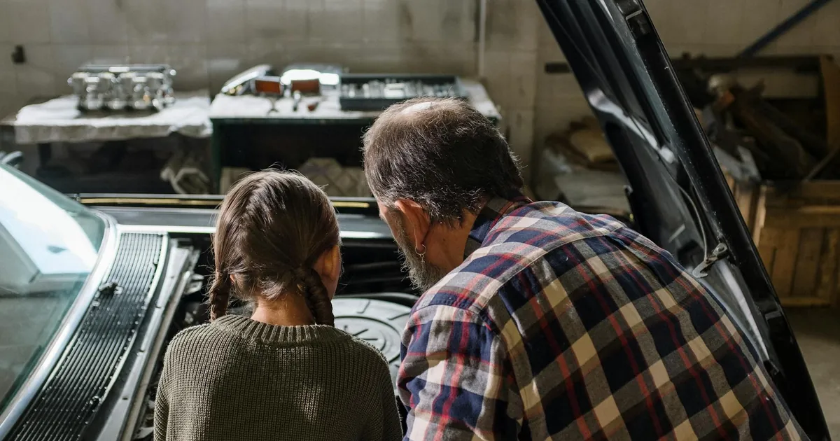 Father and daughter working together under the car hood in a cozy garage.