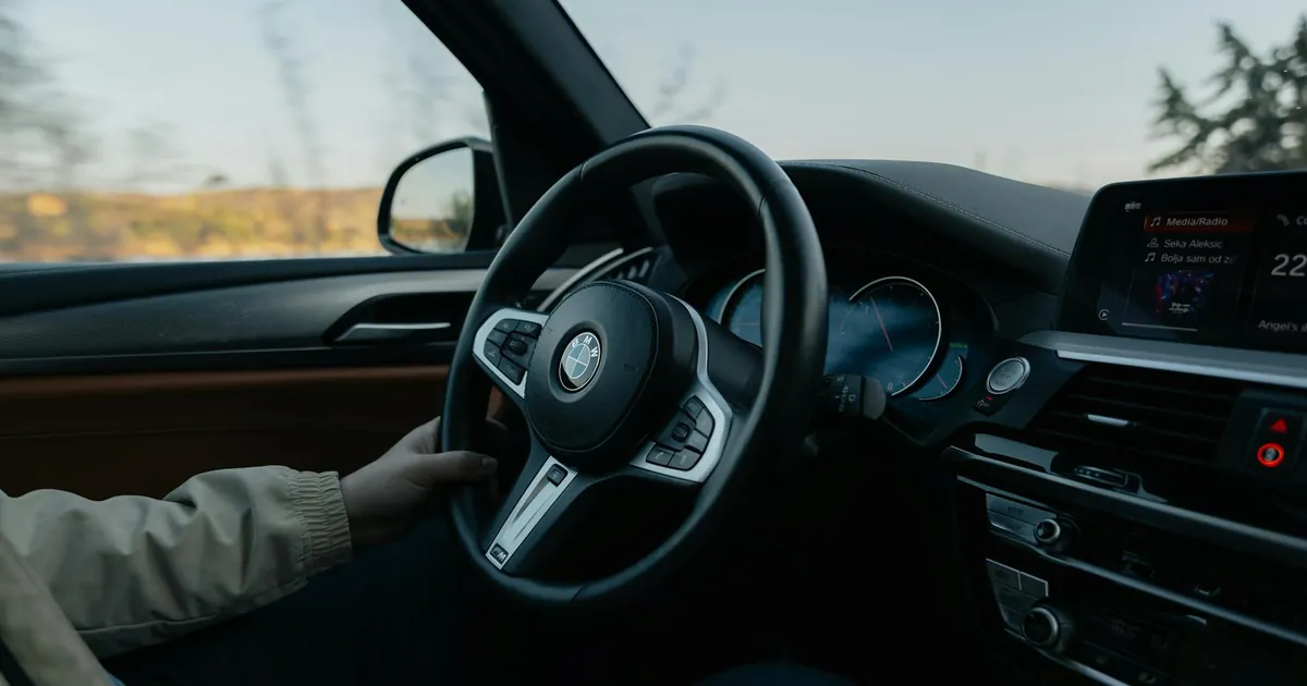 Close-up of a person driving a BMW showcasing the modern car interior during the day.