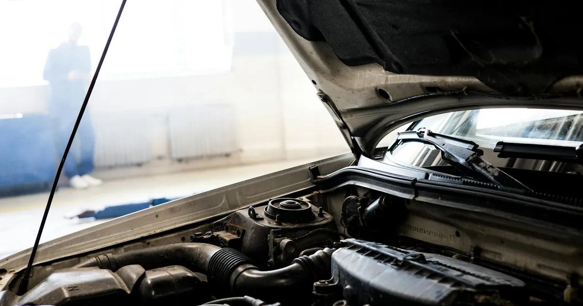 Detailed image of a car engine underneath the open hood in a well-lit indoor garage.