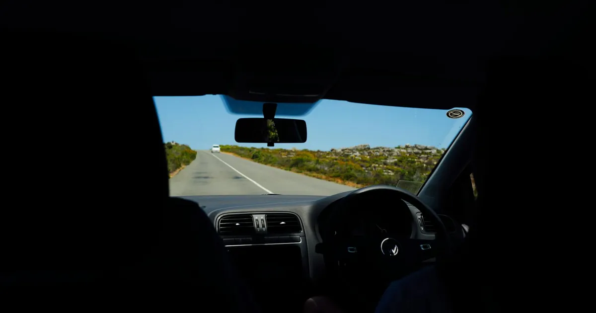 View from inside a car on a scenic road, capturing a blue sky and open road ahead.