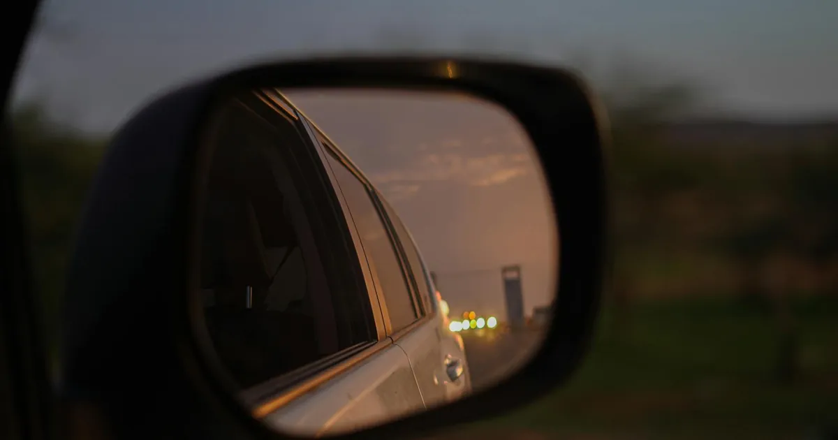 A reflective car mirror captures a scenic drive during sunset.