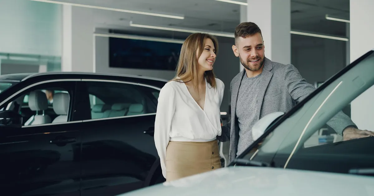 Smiling couple exploring cars at dealership, enjoying shopping experience.