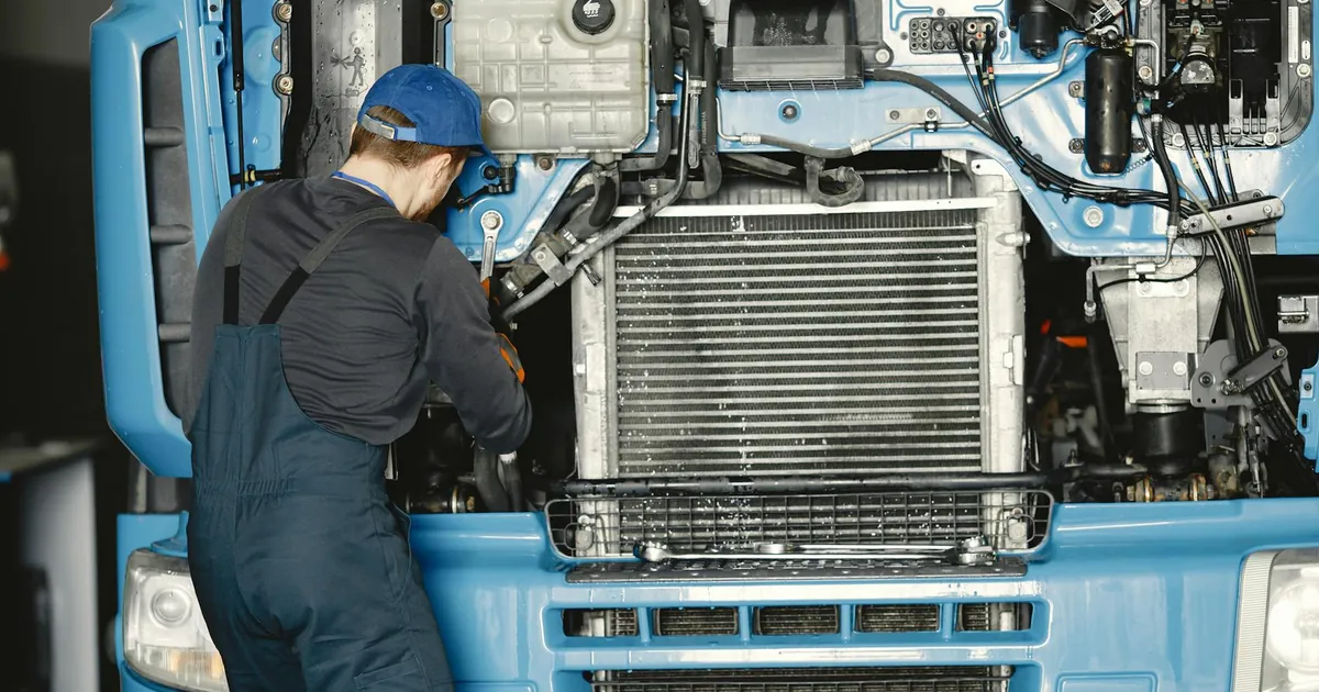 Mechanic in uniform working on a truck engine in an industrial workshop. Perfect for automotive maintenance themes.