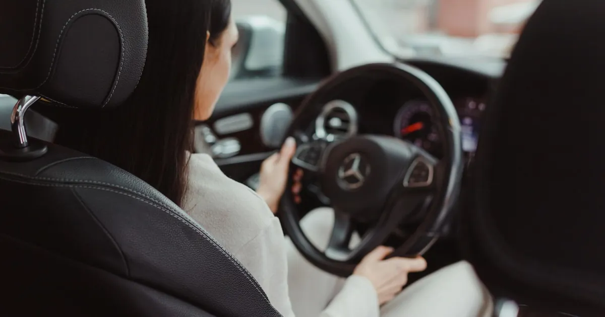 Rear view of a woman driving a Mercedes Benz, focusing on the interior and steering wheel.