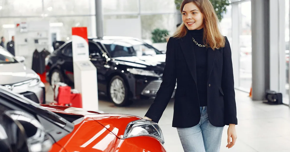 Smiling woman exploring cars in a bright showroom, expressing enthusiasm.