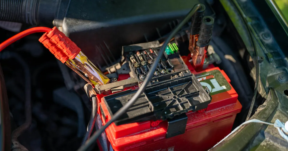 Close-up view of a car battery with red jumper cables connected, outdoors.