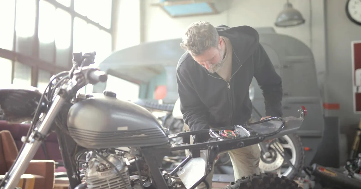 Man working on a motorcycle inside a workshop, focusing on repair and maintenance tasks.