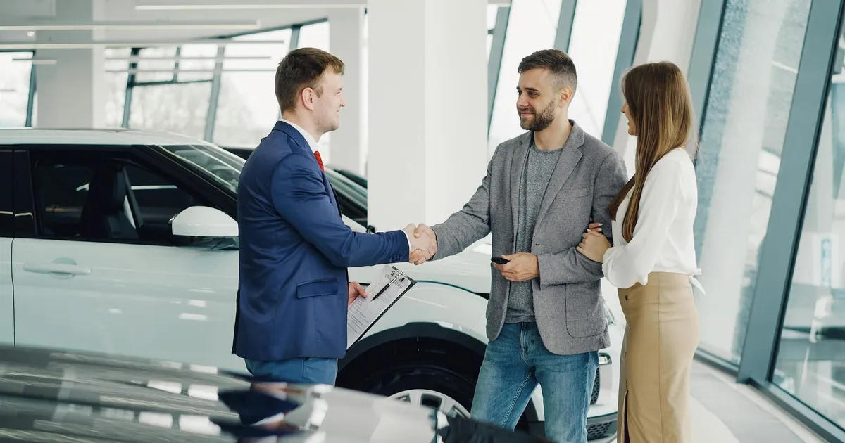 A couple completes a transaction with a salesman at a modern car dealership.