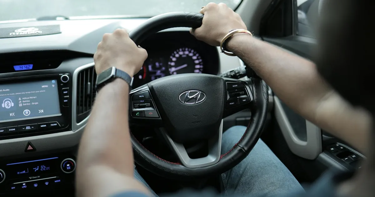 Close-up of a person's hands on a car steering wheel, highlighting the dashboard and interior features.