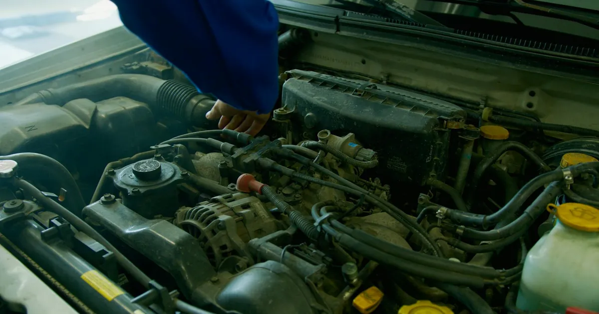 Mechanic in blue uniform working on a car engine in a garage environment.