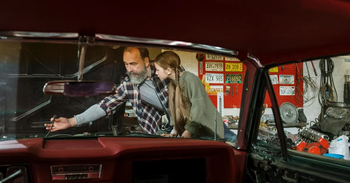 Father and daughter bonding while repairing a car together in a garage workshop. Learning and teamwork.